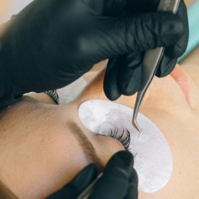 Close-up of eyelash extension application with black gloves and tweezers.